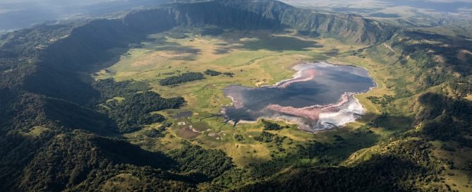 Aerial view of Ngorongoro Crater Tanzania — the world's largest intact volcanic caldera, 19 km wide, with flamingos on Lake Magadi visible on the crater floor