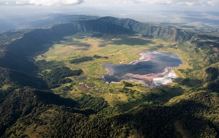 Aerial view of Ngorongoro Crater Tanzania — the world's largest intact volcanic caldera, 19 km wide, with flamingos on Lake Magadi visible on the crater floor
